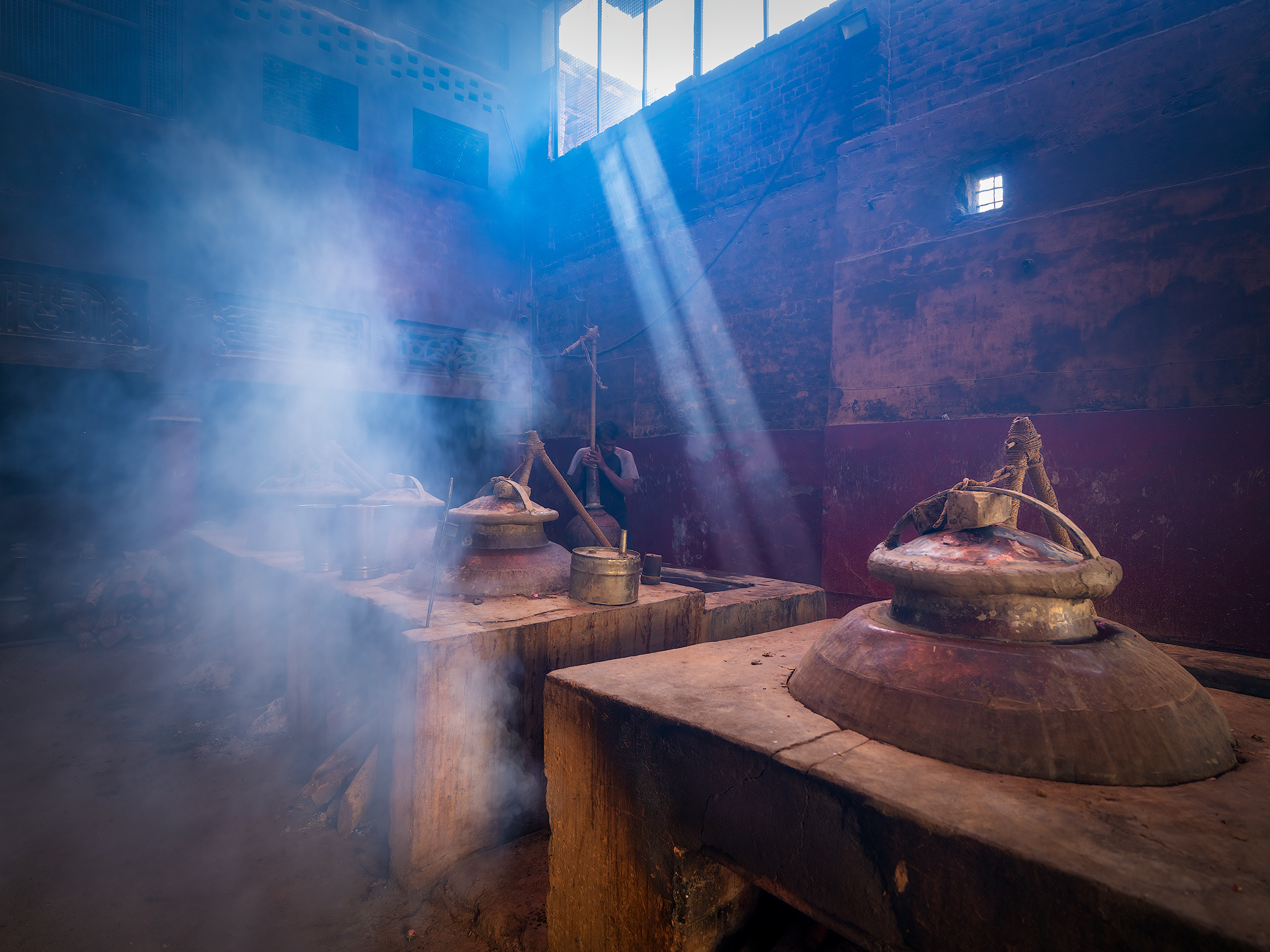 A worker at the Pranav distillery inserts the chonga, a bamboo or metal pipe that connects the deg to the bhapka and allows the aromatic vapor to pass through during distillation.
