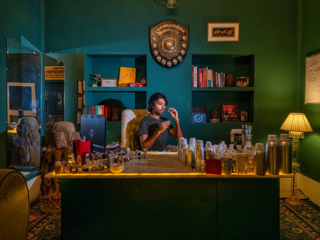 Pranav Kapoor, an eighth-generation perfumer and founder of Mitti Parfum, is deeply rooted in the tradition of perfumery in Kannauj, an Indian city renowned for its long history of distilling natural essences. In his office, Pranav spends hours testing and blending different essences, aiming to capture the soul of each ingredient. His goal is to create fragrances that are not only pleasant but also tell a story, evoking emotions and memories connected to his homeland.
His passion for perfumery is evident in the way he dedicates himself to finding the right combinations of olfactory notes. Every fragrance he develops is the result of a meticulous process that combines traditional knowledge and innovation. Pranav considers each essence as a piece of history and culture, and in his office, surrounded by bottles and tools, he works to preserve and pass on this heritage through his creations.
Moreover, Pranav has launched the “Perfume Tourism” project in Kannauj, turning his historic haveli into a place where visitors can immerse themselves in the art of traditional perfumery. During these tours, guests have the opportunity to explore distillation processes, participate in flower harvesting, and create their own personalized perfume, experiencing a unique sensory journey that celebrates Kannauj’s rich olfactory tradition.
