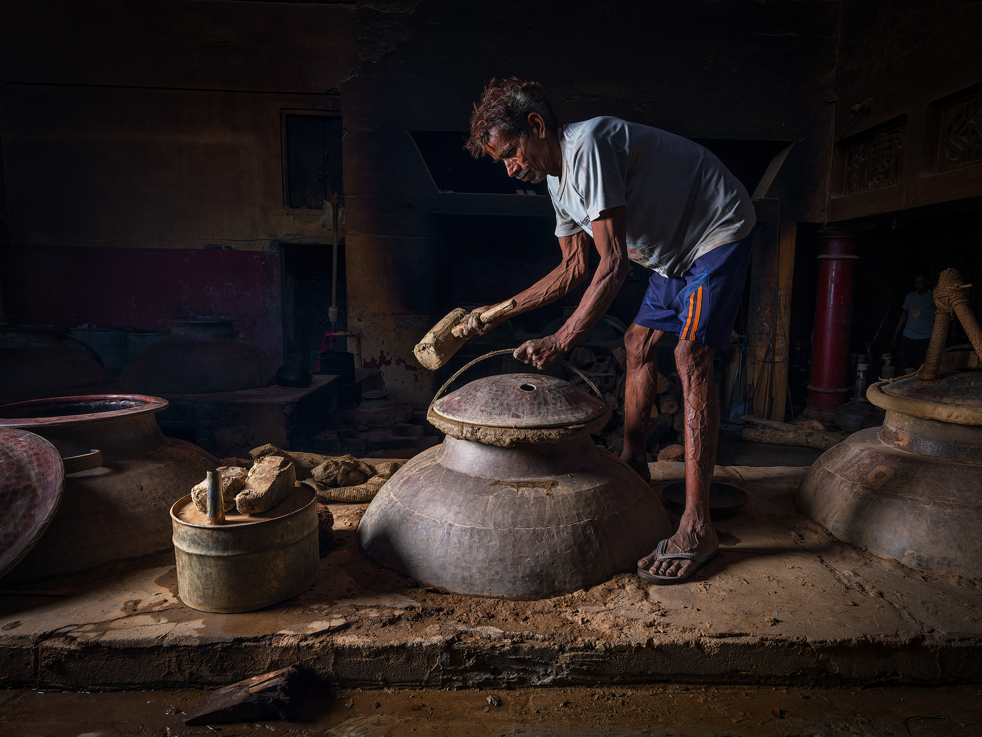 To seal the deg—the copper cauldron used in traditional distillation—a hand-prepared mixture of clay is applied just before the process begins.
The clay typically comes from local soil and has a key natural property: plasticity. This means it can be easily shaped and molded without breaking when mixed with water—similar to soft modeling clay or pottery material.
The mixture is then applied around the rim of the deg’s lid, along with wet cloth strips, to create an airtight seal. The goal is to prevent the fragrant steam from escaping during distillation, forcing it instead to travel completely through the chonga and into the bhapka, where it condenses.
Once the clay dries slightly and hardens with the heat, it forms a very effective natural seal.
At the end of the process, a hammer (hathoda) is used to break the now-dry clay crust and open the deg.