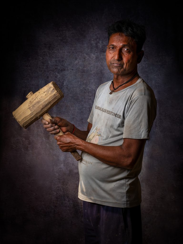 A worker with the hathoda (hammer):
A metal or wooden hammer used to secure the lid of the deg and to break the clay seal once the distillation is complete.